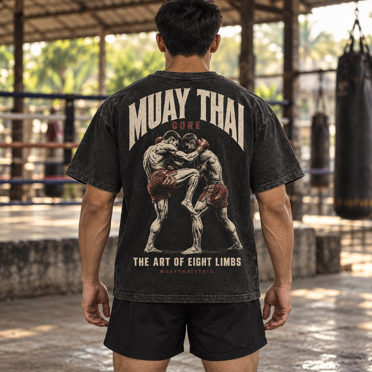 Lifestyle visualization showing the back of the Muay Thai Core tee on an anonymous model at a Thai boxing gym.